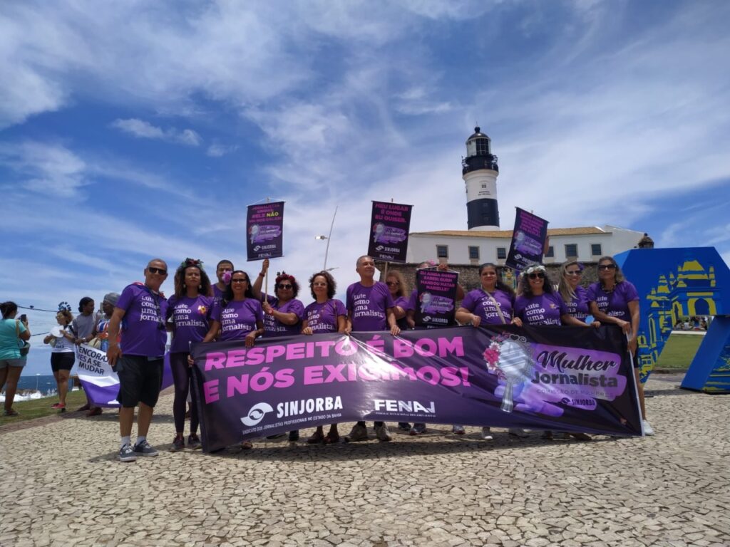 Jornalistas em frente ao farol da Barra, vestidas e vestidos com a camisa roxa "Lute como uma jornalista" e com banner em roxo referente ao 8 e março
