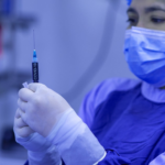 Enfermeira vestida com equipamentos de proteção individual azul segura seringa escrito "covid-19" no embolo
